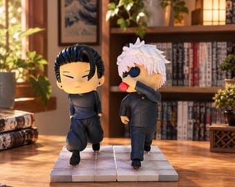 Puede incluir: Dos figuras de anime estilo chibi sobre una base de baldosas. Una figura tiene el pelo negro y uniforme azul oscuro, mientras que la otra tiene el pelo blanco, uniforme azul oscuro y una venda negra, sosteniendo un objeto rojo en la boca.