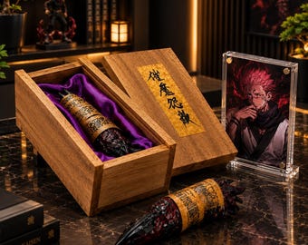 Puede incluir: Una caja de madera con forro de satén morado contiene un objeto texturizado en forma de dedo, de color rojo oscuro y dorado. Un objeto idéntico yace fuera de la caja. Un marco acrílico transparente muestra un retrato de un personaje.