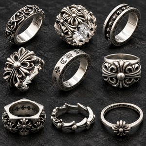 May include: A collection of nine silver rings featuring various designs including floral scrollwork, cross motifs, and engraved lettering. The rings display polished metallic surfaces with intricate detailing, ranging from wide bands to thin, delicate styles.