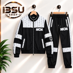 Könnte beinhalten: Ein schwarz-weißer Trainingsanzug bestehend aus einer Reißverschlussjacke und einer passenden Hose. Das Set zeigt ein wiederkehrendes MCM-Logomuster auf weißen Einsätzen an Brust, Ärmeln und Hosenbeinen. Der Text MCM ist auf Jacke und Hose gedruckt.