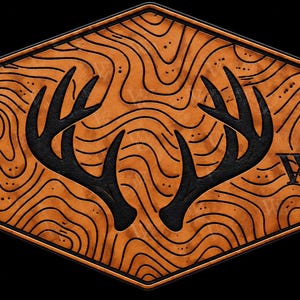 May include: A hexagonal wooden plaque featuring a natural wood grain finish with engraved black topographic contour lines. Centered on the plaque are two black deer antlers, and the letters WW are engraved in black on the lower right side.