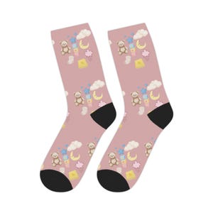 May include: A pair of dusty pink crew socks featuring a repeating pattern of brown teddy bears, yellow crescent moons, blue stars, white clouds, pink rain clouds, and yellow blocks with black heels and toes for a consistent look.