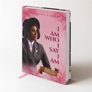 Könnte beinhalten: Ein gebundenes Buch mit dem Titel I AM WHO I SAY I AM von Toludero Adeyemi, mit einem rosa Blumenhintergrund und einem Porträt einer Person in dunklem Anzug und Hut. Ein braunes Banner unten zeigt RE-IMAGING YOUR IDENTITY mit einem rosa Lesezeichen.