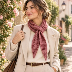 Puede incluir: Una bufanda de ganchillo color rosa empolvado con textura acanalada, atada con un nudo sencillo alrededor del cuello. La bufanda tiene extremos puntiagudos y se lleva sobre un suéter acanalado color crema y una americana beige con cinturón y bolso de cuero marrón.