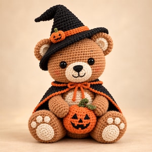 May include: A crocheted brown teddy bear wearing a black witch hat with an orange band and a small pumpkin accent. The bear wears a black cape with orange trim and holds a small orange jack-o'-lantern with a green stem in its lap.