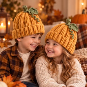 May include: Two matching pumpkin-shaped beanies made of yellow-orange yarn with a ribbed texture. Each hat features a small green crocheted stem and a curly green leaf detail on top, designed to resemble a pumpkin with a folded brim.