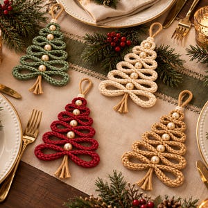 A festive table setting with four knitted Christmas tree ornaments in various colors and sizes, surrounded by candles, pine branches, and berries, creating a cozy and holiday atmosphere.