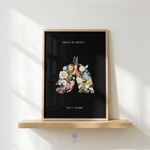 Peut inclure: Une affiche encadrée rectangulaire sur fond noir représentant des poumons humains formés par un assemblage de fleurs et de feuillages colorés. Le texte BREATH BY BREATH... et YOU'LL BLOOM. est imprimé en lettres blanches.