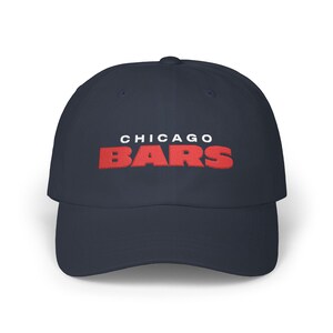 Può includere: Un cappellino da baseball blu navy con la scritta CHICAGO in lettere bianche sopra la parola BARS in grandi lettere rosse in grassetto ricamate al centro della parte anteriore. Il cappellino ha una visiera curva e sei pannelli.