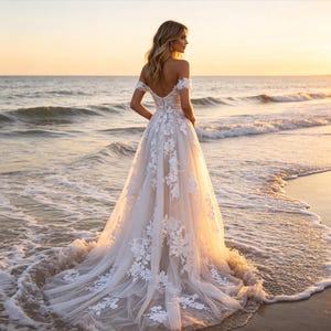Può includere: Un abito da sposa bianco lungo fino a terra con scollo a barchetta, corpetto aderente e gonna fluida decorata con intricati ricami in pizzo floreale bianco che si estendono lungo il tessuto in tulle fino all'orlo inferiore.
