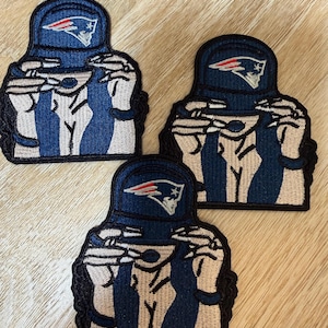 Könnte beinhalten: Drei gestickte Aufnäher mit einer stilisierten Figur, die eine blaue Baseballkappe mit einem rot-weiß-blauen Logo trägt. Die Figur hat helle Haut, dunkles Haar und hält einen kleinen Löffel an den Mund. Die Aufnäher haben einen schwarzen Rand.
