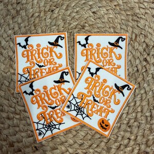 May include: Four square embroidered patches featuring the orange text Trick or Treat. Each patch includes black embroidered details of a witch hat, flying bats, a spider web, and a jack-o'-lantern pumpkin on a white background with an orange border.