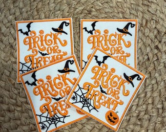 Może przedstawiać: Cztery kwadratowe naszywki z haftowanym pomarańczowym napisem Trick or Treat. Każda naszywka zawiera czarne haftowane detale przedstawiające kapelusz czarownicy, latające nietoperze, pajęczynę i dynię na białym tle z pomarańczową obwódką.