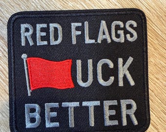 May include: A rectangular black embroidered patch with a stitched border. The text reads RED FLAGS in grey, followed by a red flag icon replacing the letter F, then UCK in grey, and the word BETTER in grey on the bottom line of the patch.