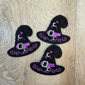 May include: Three embroidered patches shaped like pointed hats in black with purple bands, silver buckles, and white crescent moon and star accents. Each patch features a curved top and decorative purple swirl embroidery along the wide brim.