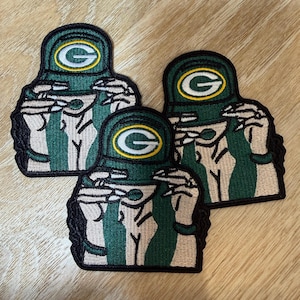 May include: Three embroidered patches featuring a stylised figure wearing a green cap with a yellow G logo. The figure has light skin, long dark hair, and is wearing a green top. Each patch has a black border and measures approximately 8 cm.