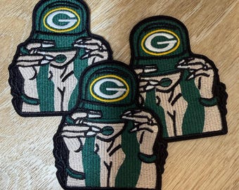 May include: Three embroidered patches featuring a stylised figure wearing a green cap with a yellow G logo. The figure has light skin, long dark hair, and is wearing a green top. Each patch has a black border and measures approximately 8 cm.