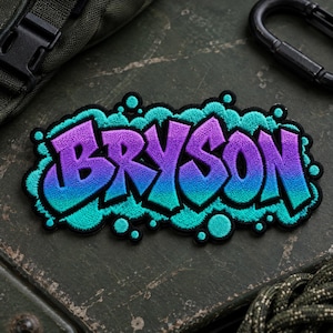 May include: An embroidered patch featuring the name BRYSON in a graffiti-style font. The letters transition from a purple top to a blue bottom, outlined in black. The entire design is surrounded by a bright teal cloud-like border with circles.