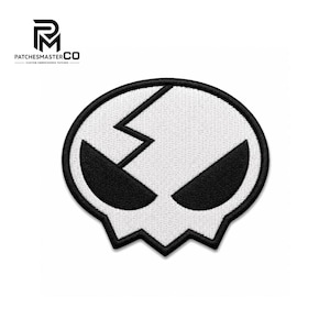 Pode incluir: Um emblema bordado apresentando uma forma de caveira branca estilizada com uma borda preta e olhos triangulares pretos. Uma linha preta irregular corre diagonalmente pela parte superior da caveira. O logotipo PATCHESMASTERCO é visível no canto superior esquerdo.