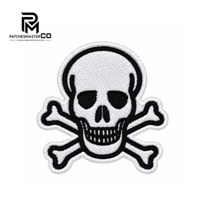 Puede incluir: Un parche bordado que presenta un diseño de calavera y tibias cruzadas en blanco con contornos negros gruesos. La calavera tiene cuencas oculares y cavidad nasal negras, con una textura cosida en blanco en toda la forma del emblema.