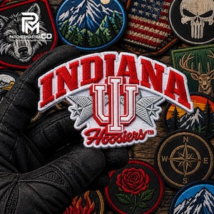 Puede incluir: Un parche bordado de los Indiana Hoosiers con el logotipo IU en rojo y blanco, la palabra INDIANA en letras rojas de bloque y la palabra Hoosiers en letra cursiva roja. El diseño incluye dos estrellas plateadas sobre fondo blanco y bordes rojos.