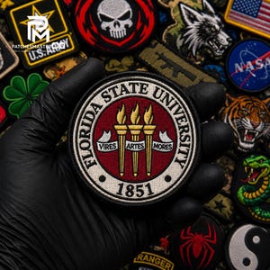 May include: A circular embroidered patch featuring the Florida State University seal. The design includes three gold torches on a maroon background, surrounded by a white border with the text Florida State University and the year 1851.