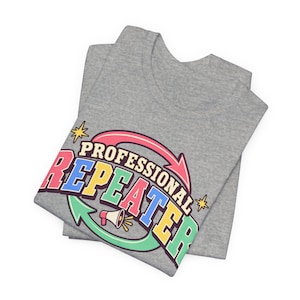 Peut inclure: Un t-shirt gris chiné arborant un graphisme coloré avec le texte "PROFESSIONAL REPEATER" dans une police audacieuse et multicolore. Le motif comprend une flèche rose, une flèche verte, de petites étoiles jaunes et une icône de mégaphone.