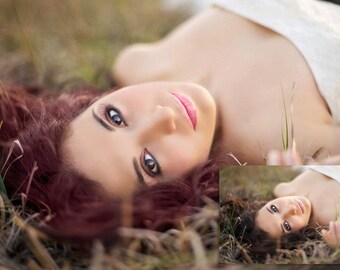 May include: A woman with long, dark red hair lies on her back in a field of dry grass. She is wearing a white strapless dress and has her eyes closed. The sun is shining on her face, and she looks peaceful and relaxed.