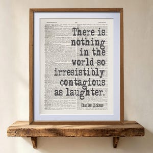 Może przedstawiać: Oprawiony wydruk artystyczny z cytatem There is nothing in the world so irresistibly contagious as laughter autorstwa Charlesa Dickensa, nadrukowany na tle strony ze starego słownika z czarnym tekstem w drewnianej ramie.