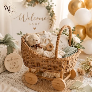 May include: A woven wicker baby carriage basket containing a crocheted teddy bear with a brown ribbon, a wooden teether, white knitted booties, a folded sage green cloth, and a card with the text Hello BABY, set on a round woven mat.