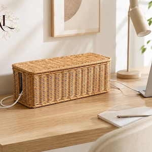 May include: A rectangular light brown woven rattan cable management box with a removable lid. The box features a vertical side opening for cords to pass through, designed to conceal power strips and electrical cables on a desk surface.
