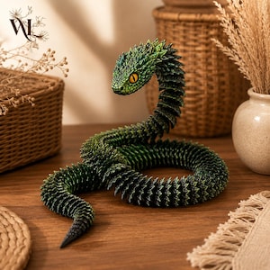 May include: A green articulated snake figurine with a textured, scale-like body and a raised head. The snake features a gradient of dark to light green colouring, a pointed tail, and a single visible eye with a bright yellow iris and black pupil.