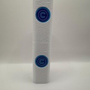 May include: A tall, cylindrical white object with a textured surface. It features two circular blue emblems stacked vertically, each displaying a stylised letter C in the centre surrounded by concentric rings. The design is clean and symmetrical.