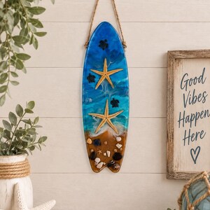 Handgemaakte wanddecoratie van hars in de vorm van een surfplank, met zeeschildpad en zeester als strandkunst.