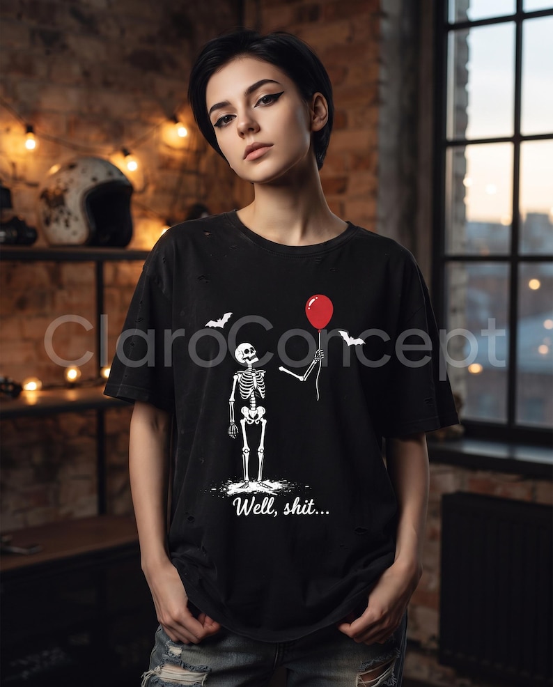 May include: A black t-shirt featuring a graphic of a white skeleton holding a single red balloon. The design includes two small white bats and the text "Well, shit..." printed in white below the skeleton. The fabric has a distressed, worn look.