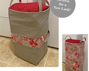 May include: A reversible fabric laundry hamper with two handles. One side is solid light gray with a horizontal band featuring a red floral pattern. The other side is primarily red floral fabric with a solid light gray base. Text reads: Reverse for a New Look!