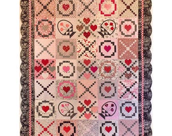 May include: A rectangular quilt featuring a grid of squares with heart motifs, floral patterns, and geometric designs in shades of red, pink, white, and black. The quilt is finished with a scalloped black border and a thin red and white checkered trim.