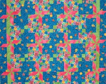 May include: A patchwork quilt featuring a repeating pattern of blue fabric squares with small yellow suns and pink diagonal strips. Interspersed are blocks of multi-colored floral fabric in shades of pink, yellow, and green, all framed by lime green borders.