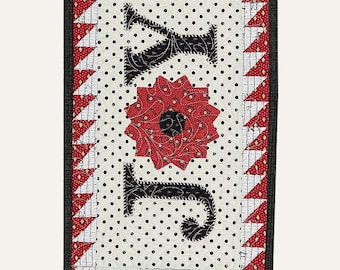 May include: A rectangular wall hanging quilt featuring the word JOY in black fabric letters on a cream background with black polka dots. A red and white patterned border surrounds the center, framed by a dark grey edge. Text reads #287, 8 1/2" x 14 1/2", SUZN QUILTS, and Sewing with Susan.