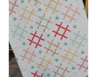 May include: A white quilt featuring a repeating pattern of hashtag symbols in various colors including red, yellow, peach, and light green. The fabric has a textured, swirling quilted design throughout, with small solid green squares between symbols.