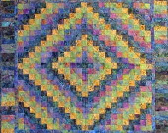 May include: A square quilt featuring a central diamond pattern composed of small, multi-colored fabric squares in shades of blue, purple, green, and yellow. The quilt is framed by a wide border of vertical rectangular fabric strips.
