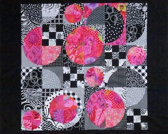 May include: A square quilt featuring a black border and a central grid of alternating black and white geometric patterns, including stripes, checkers, and circles. Several large, vibrant pink floral-patterned circles are layered over the grid.