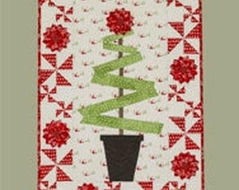 May include: A quilt pattern titled Lollipop Tree #272 by Suzn Quilts. The design features a central green ribbon tree in a black pot, surrounded by a border of red and white pinwheel and floral blocks. The finished size is 23 inches by 36.5 inches.