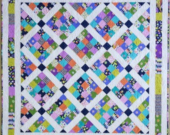 May include: A square quilt featuring a grid of diamond-shaped blocks composed of multi-colored fabric squares in shades of orange, purple, green, and blue. The blocks are separated by white sashing and dark blue cornerstones, with a pieced border.