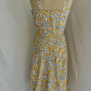 K&ouml;nnte beinhalten: Ein Kleid im Vintage-Stil mit gelbem Hintergrund und einem sich wiederholenden Muster aus wei&szlig;en, schwarzen und t&uuml;rkisfarbenen Formen. Das Kleid hat einen quadratischen Ausschnitt, d&uuml;nne Tr&auml;ger und ein eng anliegendes Oberteil. Der Rock verl&auml;uft von der Taille aus.