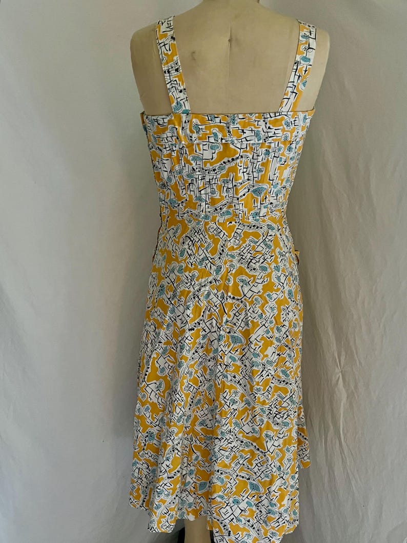 K&ouml;nnte beinhalten: Ein Kleid im Vintage-Stil mit gelbem Hintergrund und einem sich wiederholenden Muster aus wei&szlig;en, schwarzen und t&uuml;rkisfarbenen Formen. Das Kleid hat einen quadratischen Ausschnitt, d&uuml;nne Tr&auml;ger und ein eng anliegendes Oberteil. Der Rock verl&auml;uft von der Taille aus.