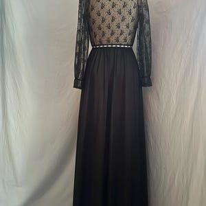 May include: A black formal dress with a high neckline and long sleeves. The bodice and sleeves are sheer, patterned lace. The waist is defined with a white trim. The skirt is a flowing, solid black fabric.