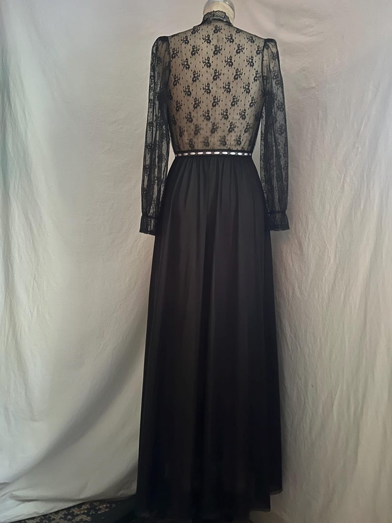 May include: A black formal dress with a high neckline and long sleeves. The bodice and sleeves are sheer, patterned lace. The waist is defined with a white trim. The skirt is a flowing, solid black fabric.