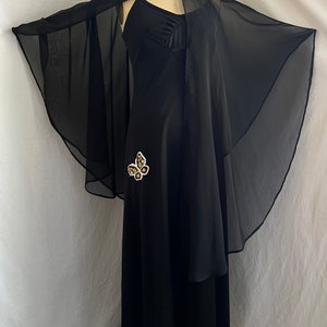 May include: A black maxi dress with a sheer black cape and a gold butterfly embellishment.