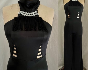 Puede incluir: Mono negro con cuello alto y detalle de flecos. El mono tiene aberturas en los lados y una pierna ancha.